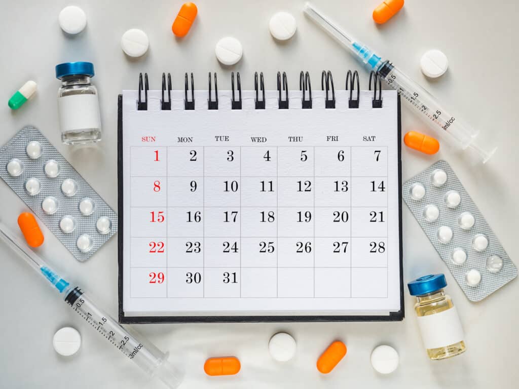 Syringes, injection vials and a calendar page lying on the table. Close-up, indoors, top view. Day light, studio photo. Healthcare concept